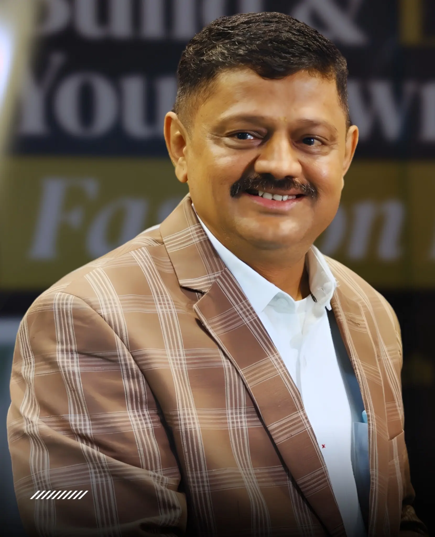 Satyanarayana Sheshagiri, smiling, in a checked blazer over a white shirt, photographed against a blurred event backdrop
